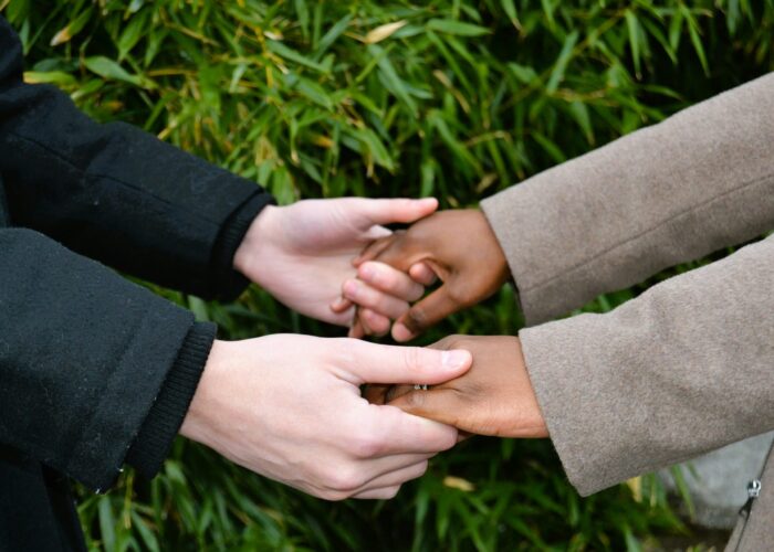Two people holding hands outdoors, wearing coats, with green leaves in the background.