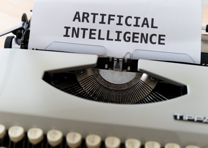 A typewriter with a sheet of paper displaying ARTIFICIAL INTELLIGENCE in uppercase letters.