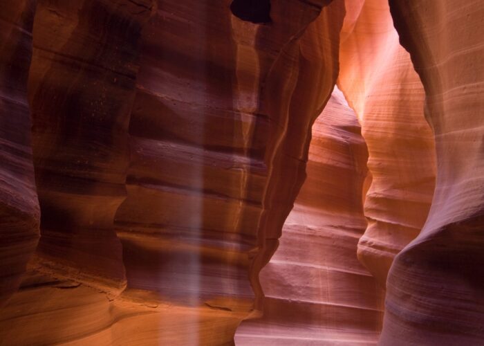 Sunlight beams through narrow, wavy rock formations in a sandstone slot canyon.