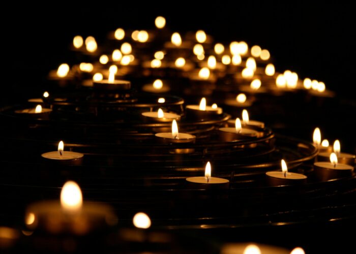 Numerous candles glow softly in a dark setting, creating a warm and serene atmosphere.