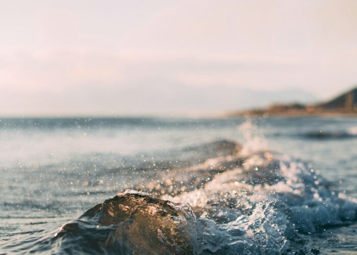 Gentle waves crashing on the shore under a clear sky, with distant mountains in the background.