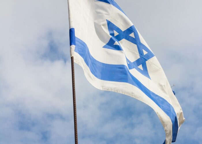 Israeli flag with blue Star of David and stripes waving against a cloudy sky.