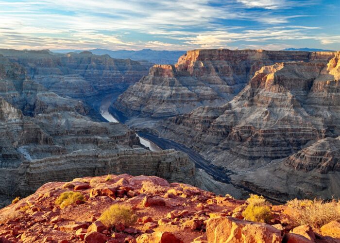 Vista of the Grand Canyons layered rock formations and winding river under a partly cloudy sky.