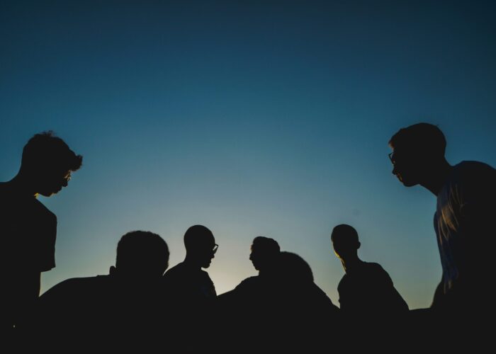 Silhouettes of six people standing together against a clear blue sky at sunset.