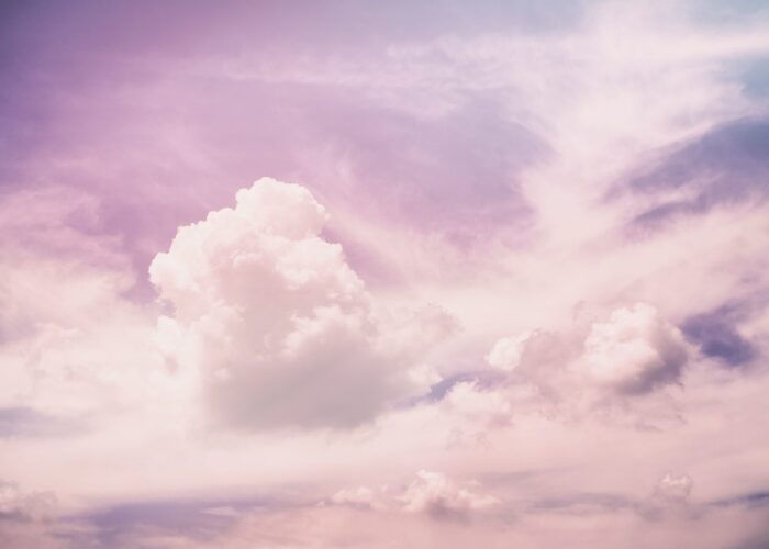 Pink-tinted sky with fluffy white clouds scattered across various shades of light blue and lavender background.