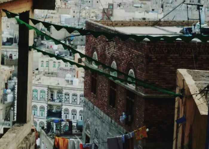 Narrow alleyway with colorful clothes hanging, brick buildings, and a hilly cityscape in the background.