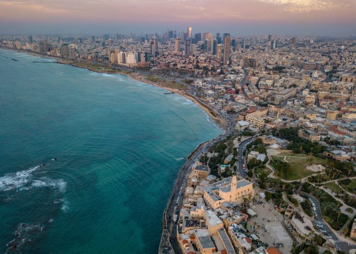 Aerial view of a coastal city with skyscrapers, historic buildings, and a sprawling beach beside turquoise sea.