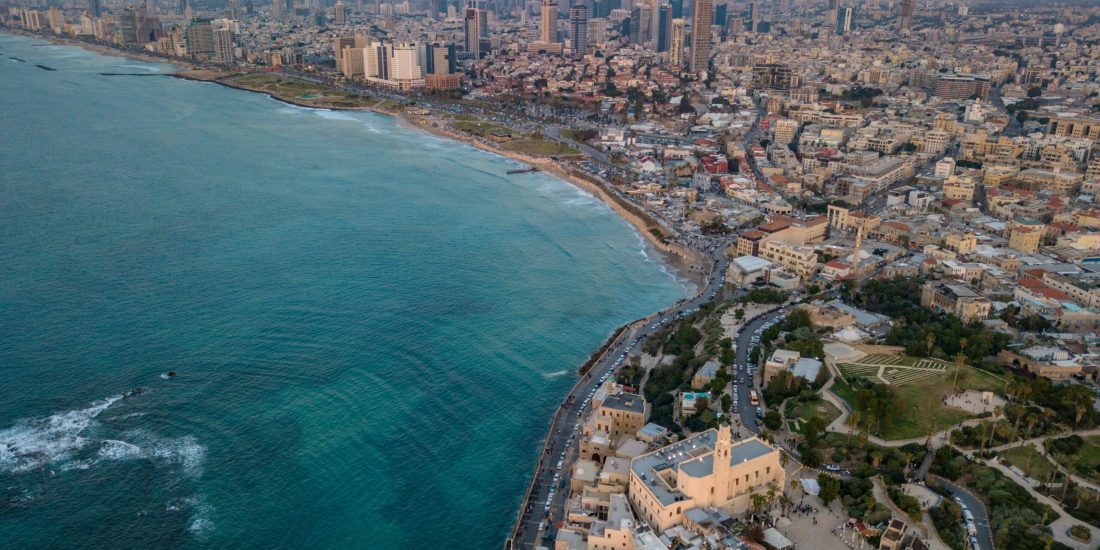 Aerial view of a coastal city with skyscrapers, historic buildings, and a sprawling beach beside turquoise sea.