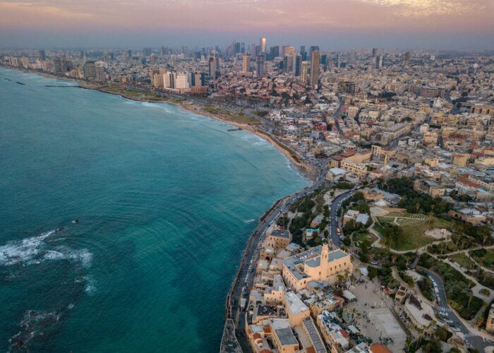 Aerial view of a coastal city with skyscrapers, historic buildings, and a sprawling beach beside turquoise sea.