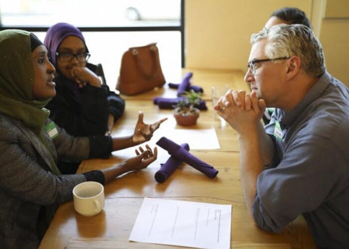 A diverse group of people sitting at a table in a discussion, with papers and a coffee cup in view.
