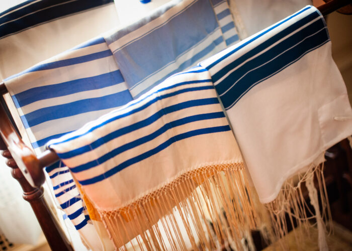 Colorful prayer shawls with blue stripes are draped over a wooden rack.