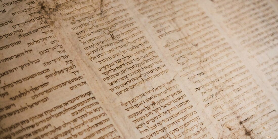 A close-up of an old, dusty Hebrew manuscript with faded, vertical columns of text.