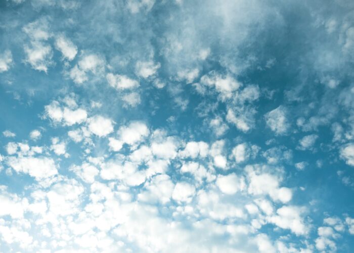 Fluffy white clouds scattered across a bright blue sky on a sunny day.