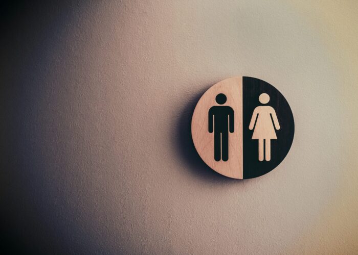 A circular restroom sign showing male and female symbols on a textured wall.