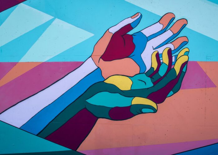 Colorful mural of two outstretched hands against a background of geometric shapes in shades of blue, orange, and pink.