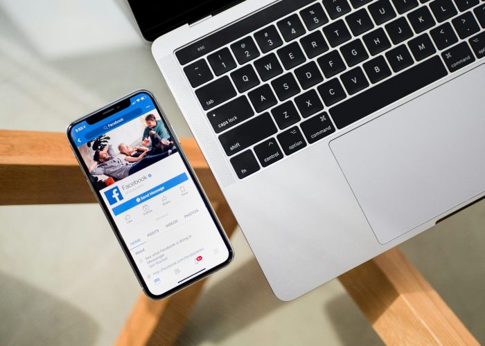 Smartphone displaying Facebook app on a table next to an open laptop.