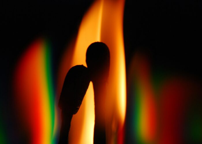 Silhouettes of two matchsticks with a colorful, blurred flame background.