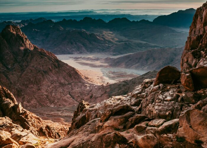 Rocky mountain landscape with a valley below under a dramatic sky at sunrise or sunset.