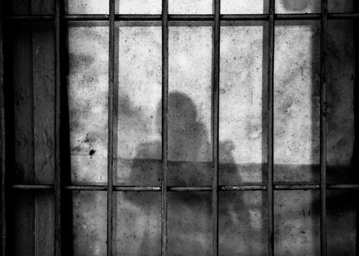 Shadowy figure behind a barred, dirty window, creating a mysterious and eerie atmosphere.